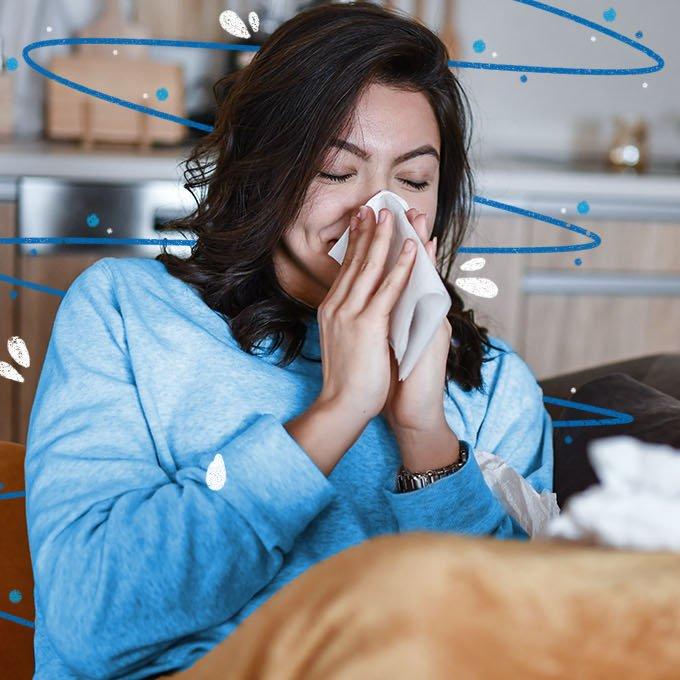 Someone blowing their nose into a tissue with closed eyes