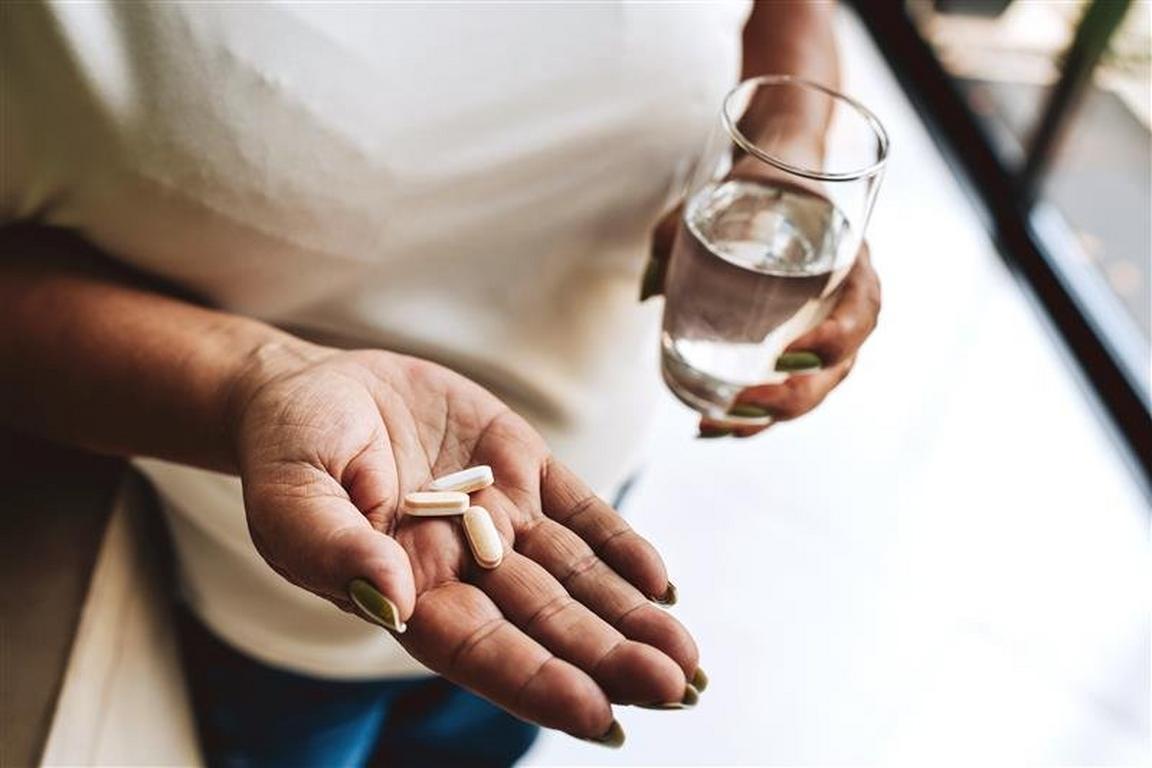 A person's hands holding pills and a glass of water