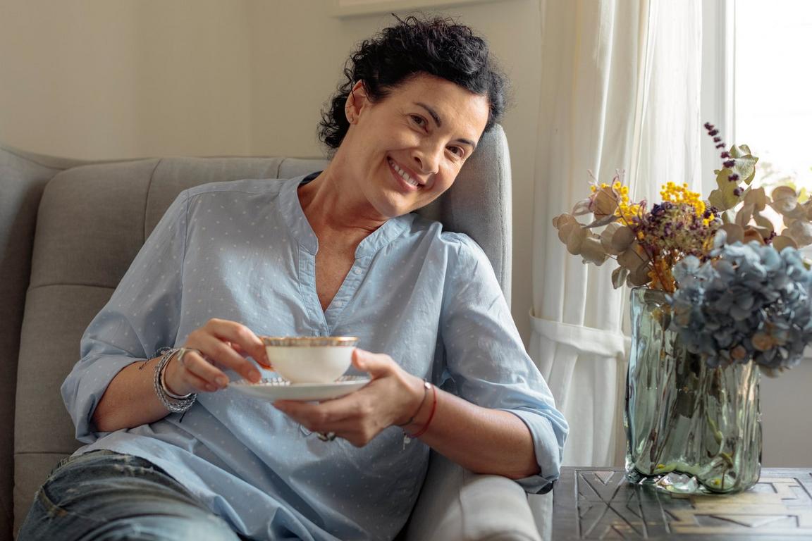 A women smiling, sat on a chair holding a cup