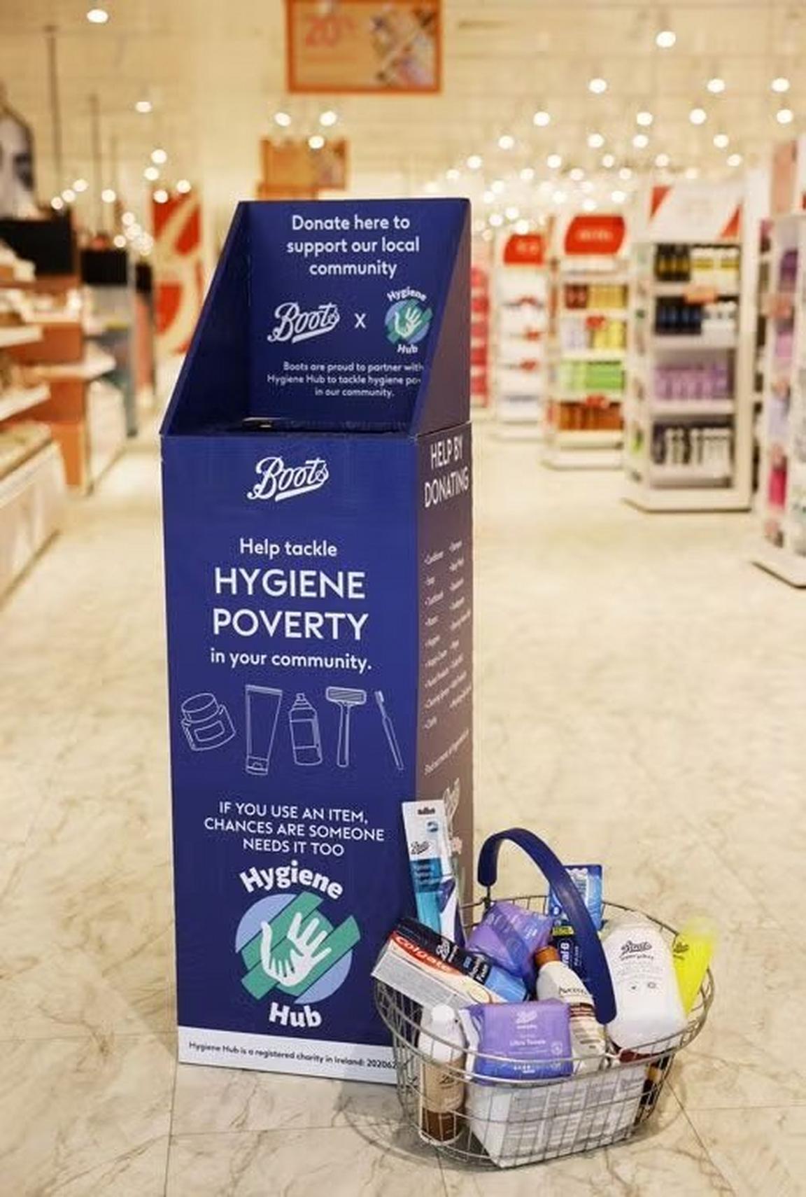 A blue donation bin for hygiene products with a shopping basket full of items in a retail store.