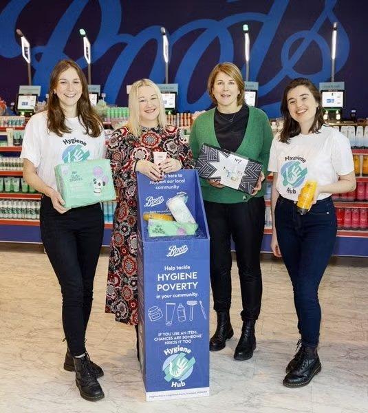 Four women posing with hygiene products and a donation box in a store.