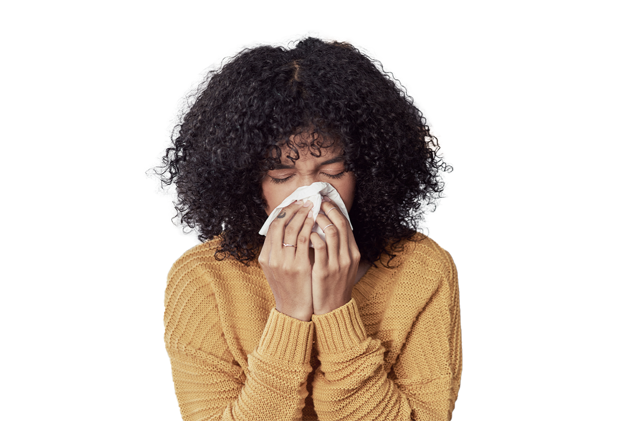 Person with curly hair in a yellow sweater holding a tissue to their nose on a gray sofa.