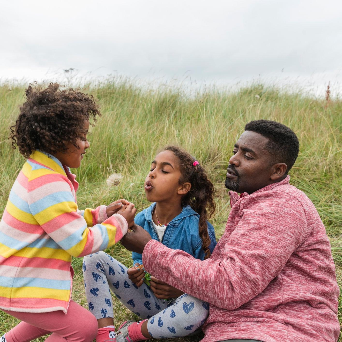 An adult and 2 young children sat on a grass banking together