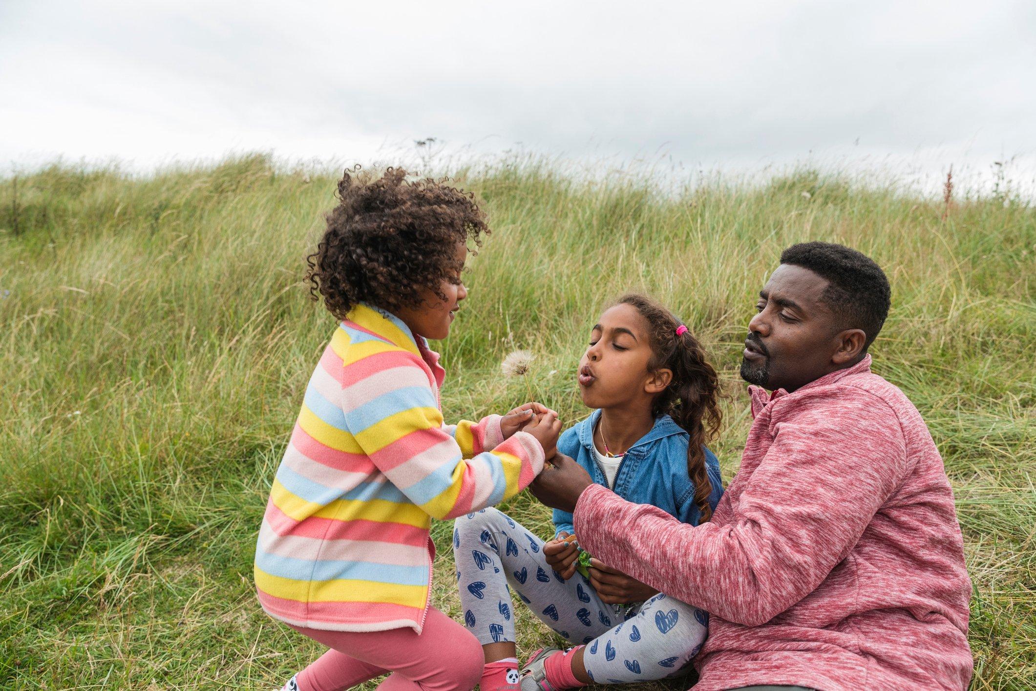 Children and an adult playing with a dandelion in a grassy field.