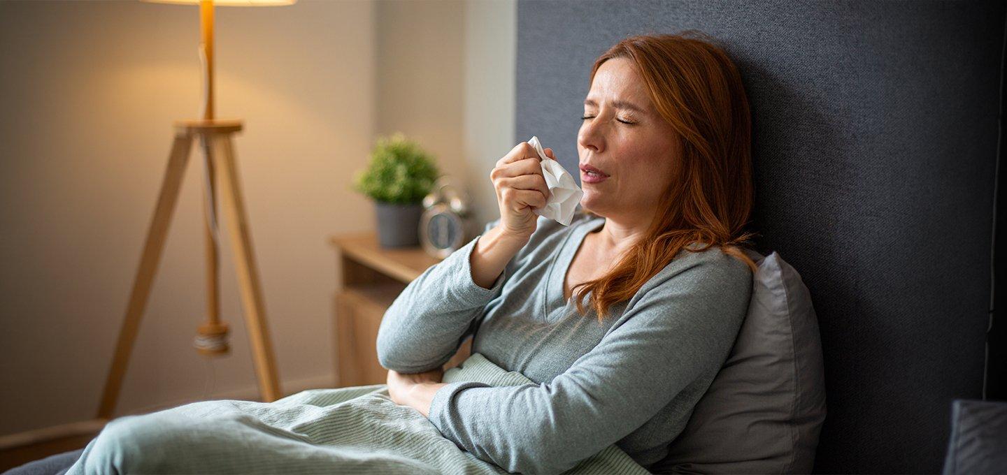 Person in bed using a tissue in a bedroom setting.