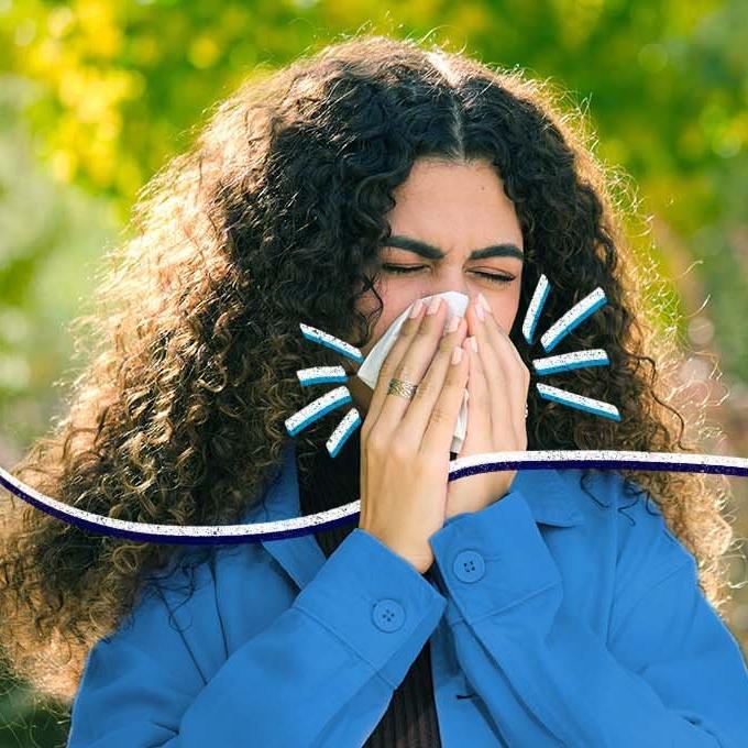 Person sneezing into a tissue outdoors with curly hair and a blue outfit