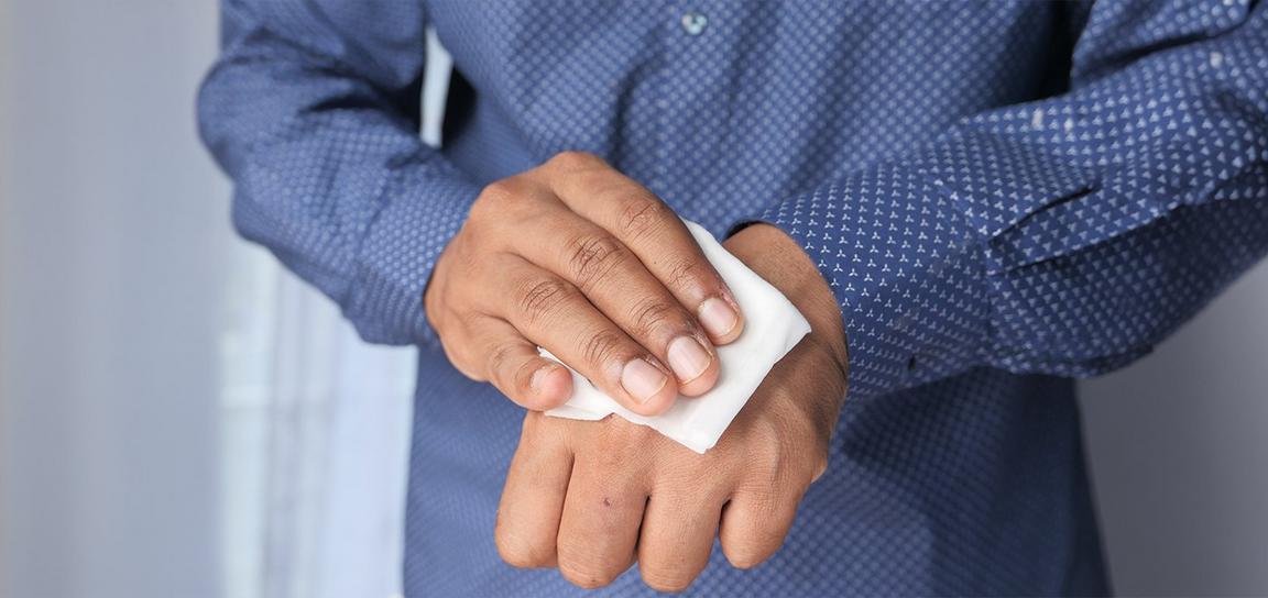 A close-up of a person’s hand using a tissue to clean the back of their wrist while wearing a blue shirt with a white triangle pattern.