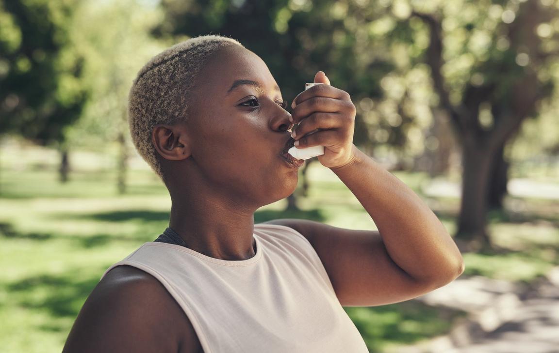 A person in a park using an inhaler on a sunny day.