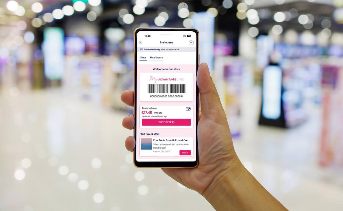 A hand holding a smartphone displaying a digital rewards card in a store environment.