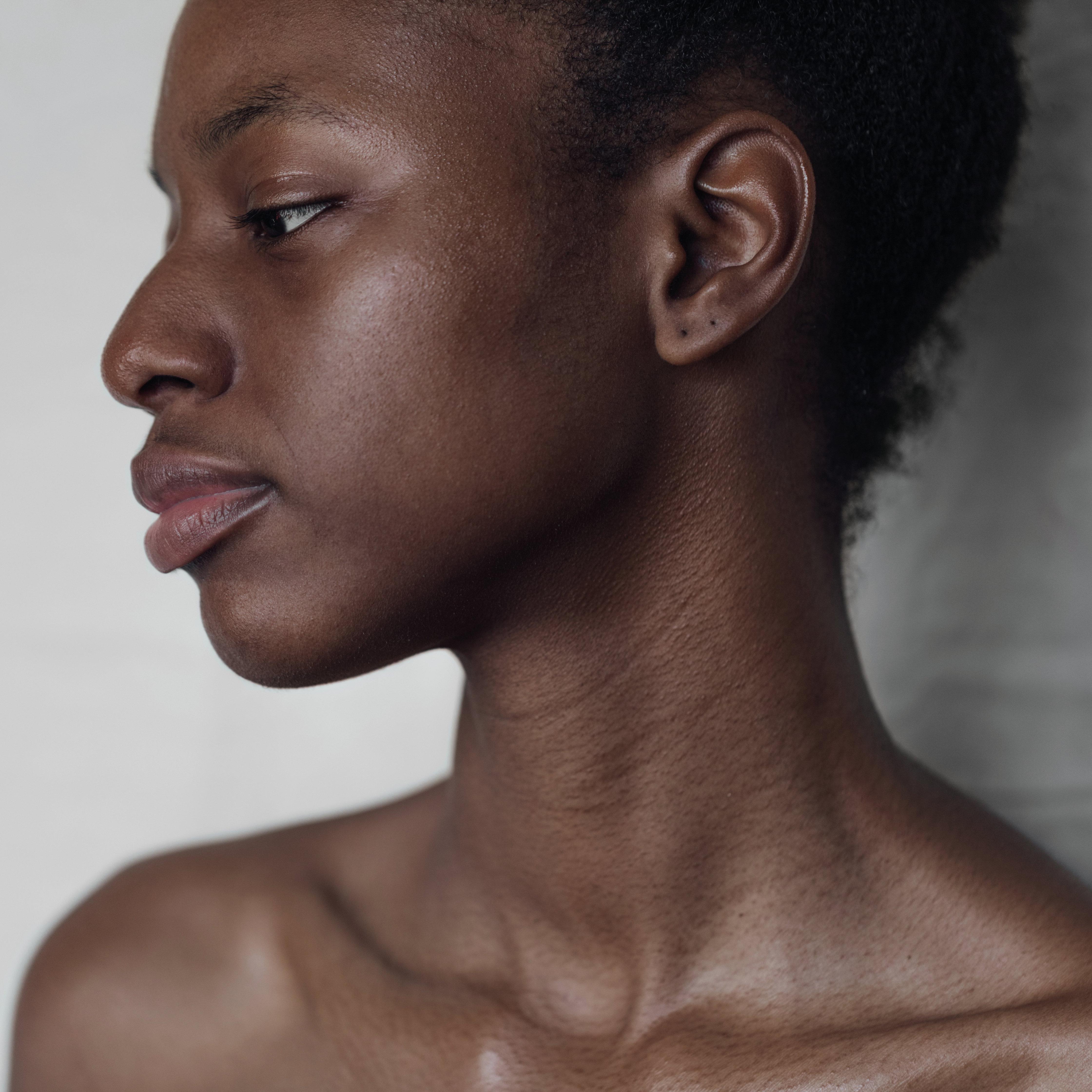 Close-up profile of a person facing left with a serene expression against a gray background.