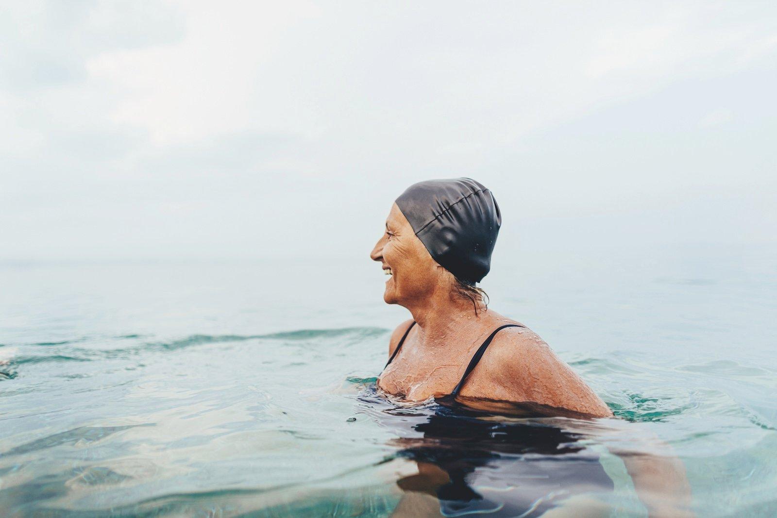Person wearing a swim cap in water, smiling and looking to the left.