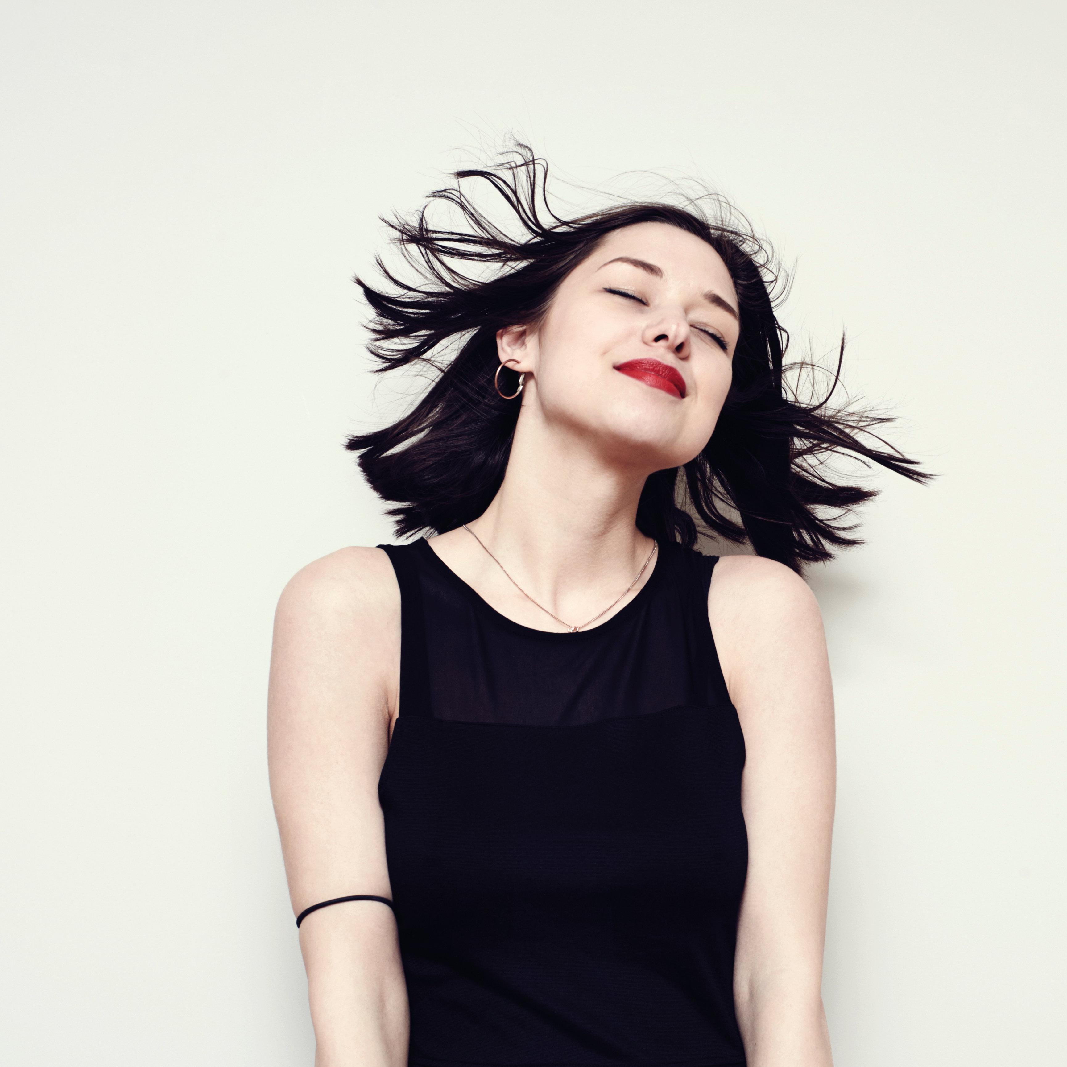A woman with dark hair smiling with her eyes closed