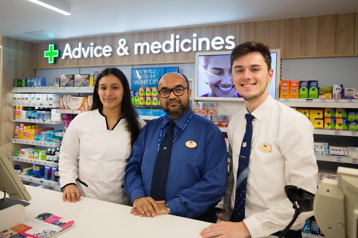 Three people standing behind a pharmacy counter under a sign that reads "Advice & medicines."