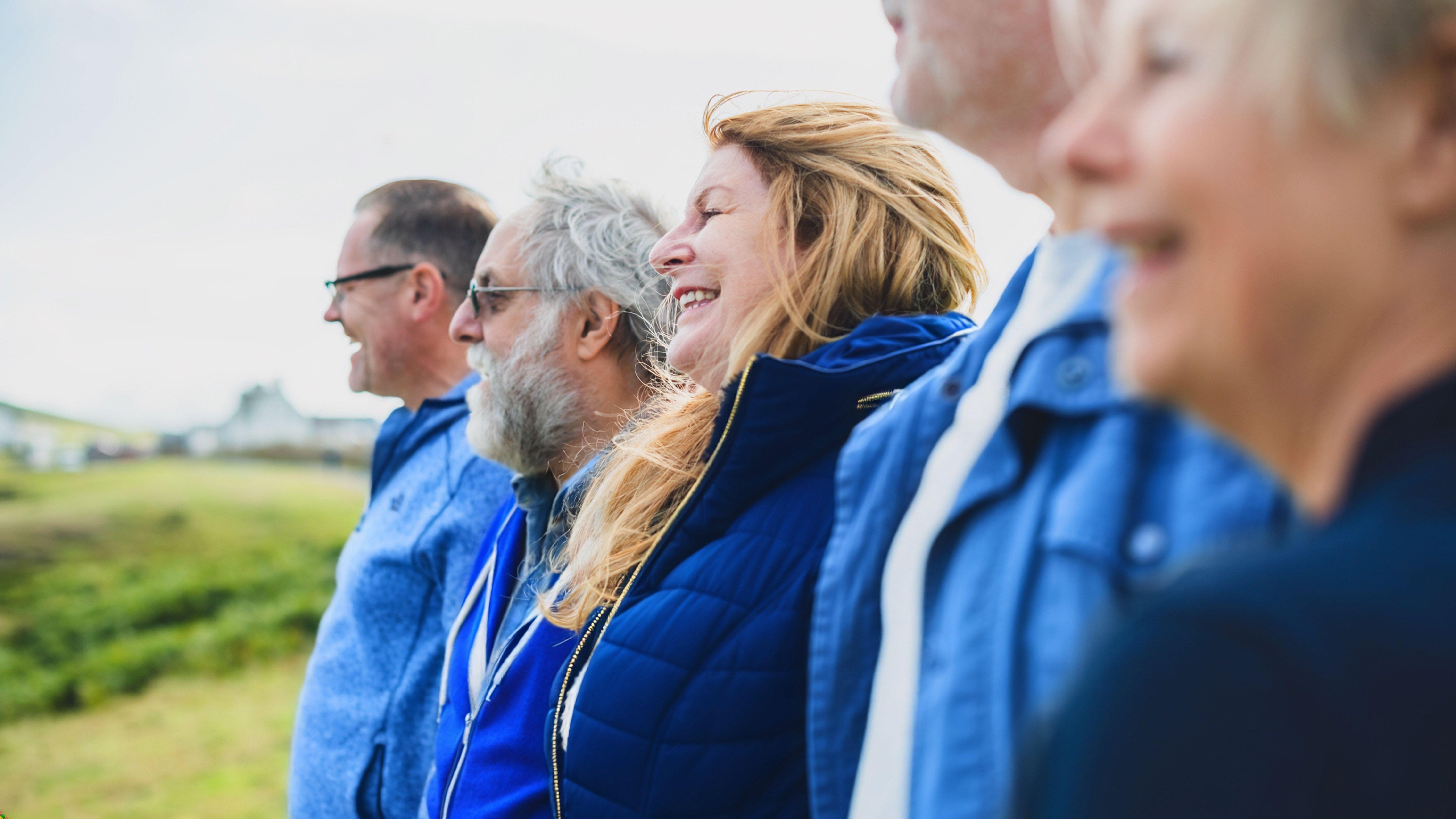 Group of five people in blue clothing standing outdoors, with a green landscape in the background.
