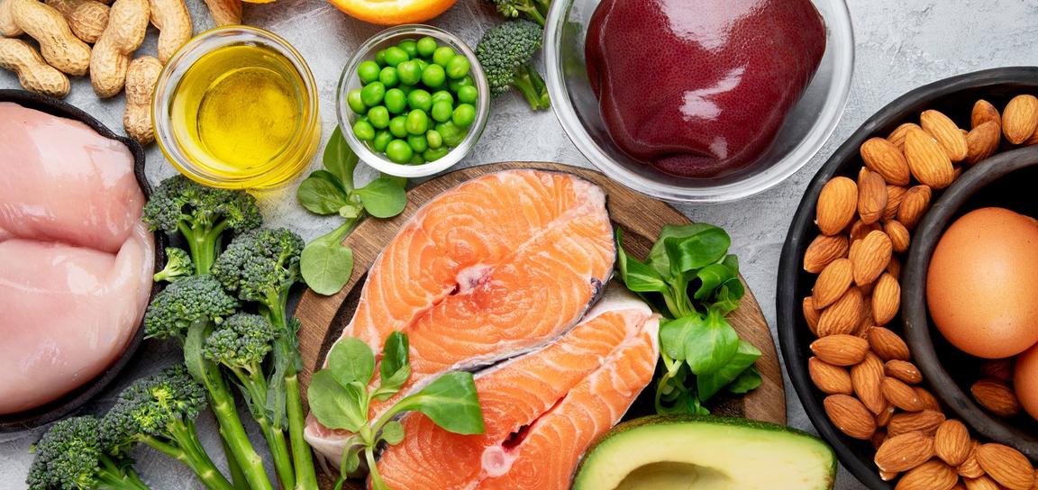 An arrangement of fresh foods includes salmon, chicken breasts, broccoli, almonds, and eggs, creating a colorful and nutritious display.