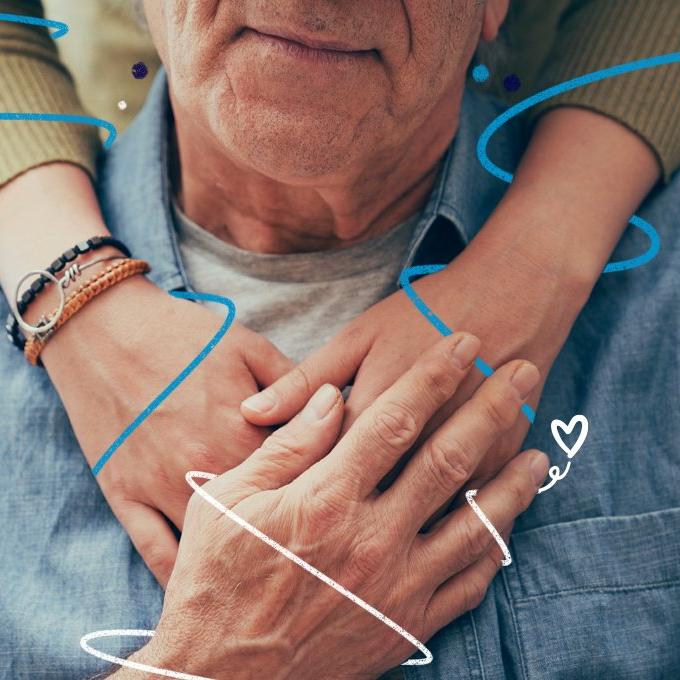 A person sat down with someone stood behind them with their arms over their shoulders