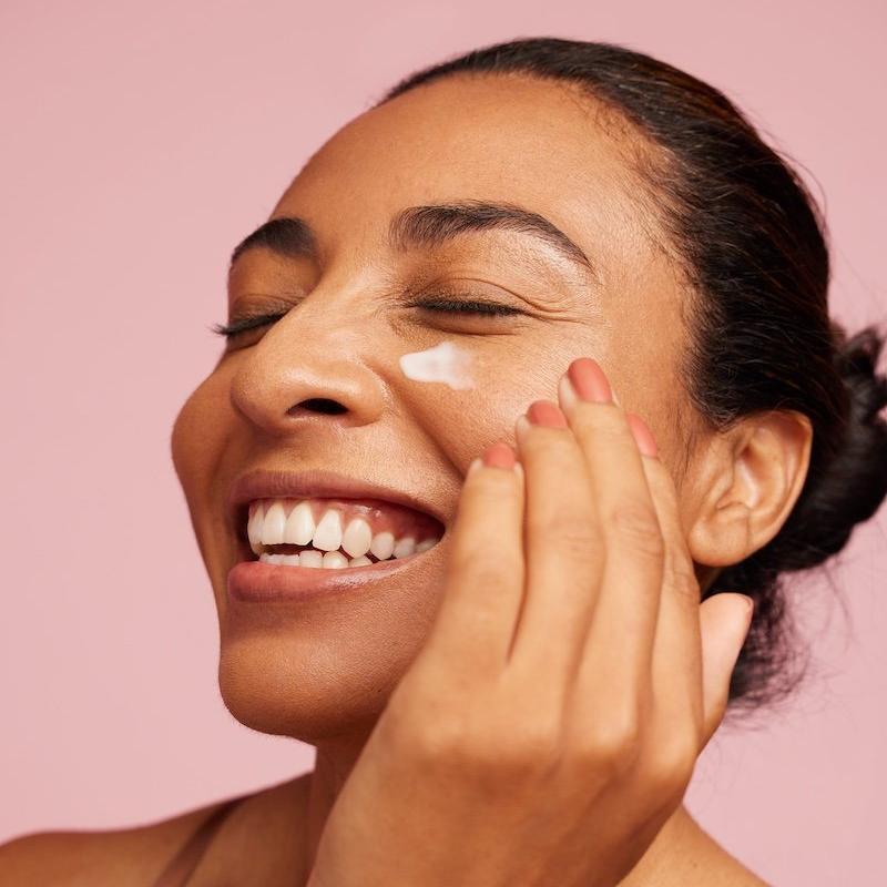 A woman smiling while applying moisturiser to her skin