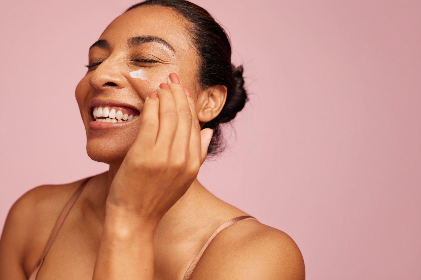 A woman smiling while applying moisturiser to her skin