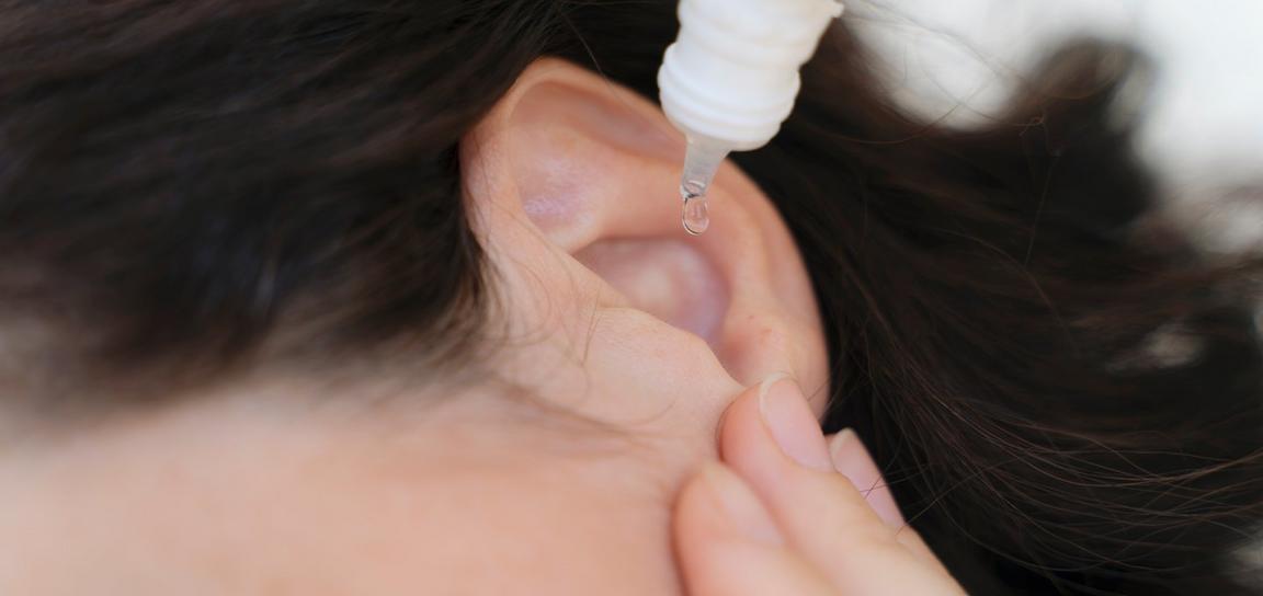 Close-up of a liquid dropper administering a droplet into an ear.