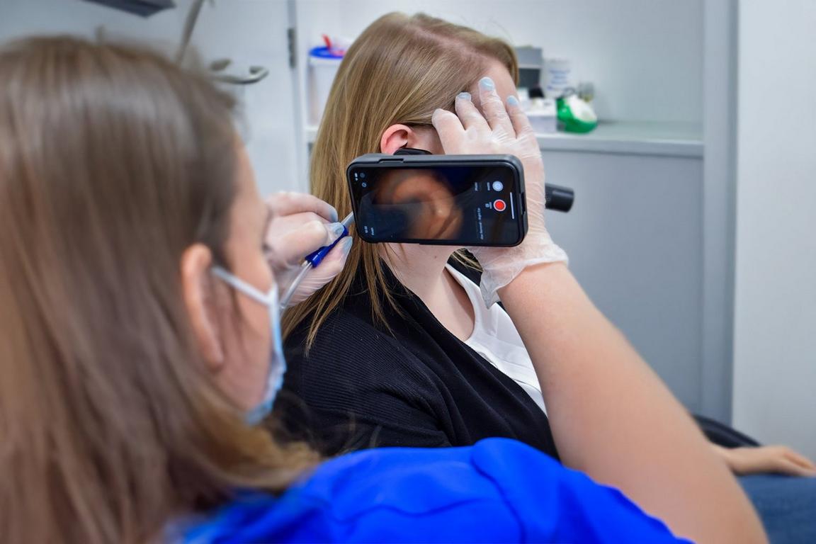 A doctor holding a camera and a medical tool to clean out the inside of a person's ear