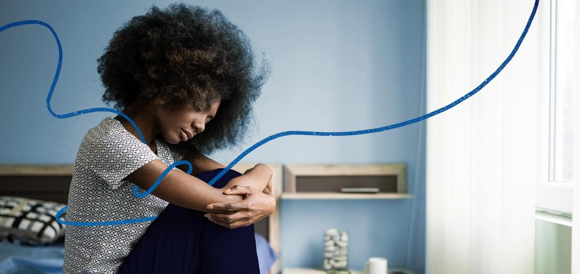 Someone sat on a bed holding their knees to their chest