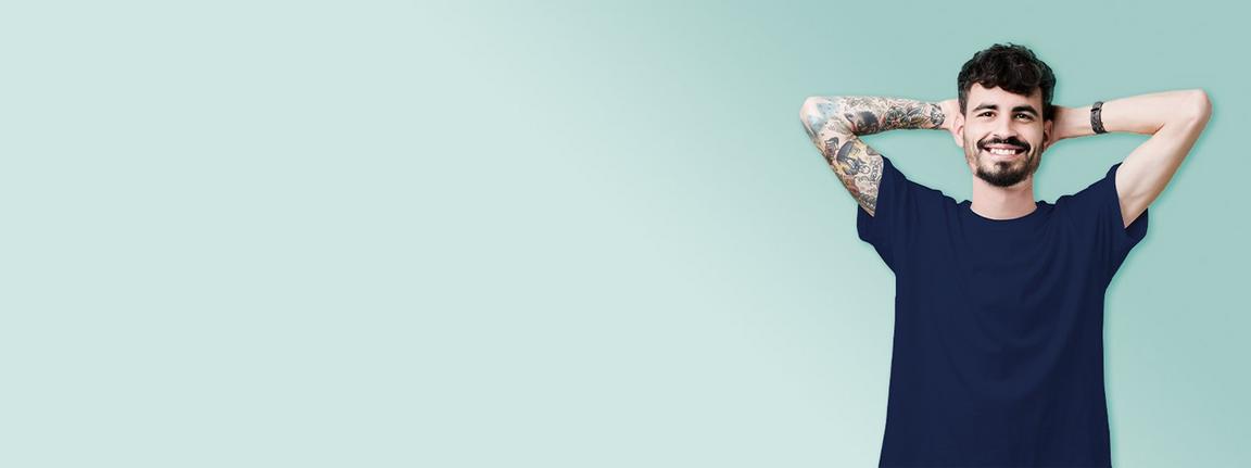 A man with dark hair and tattoos with his hands behind his head against a teal background