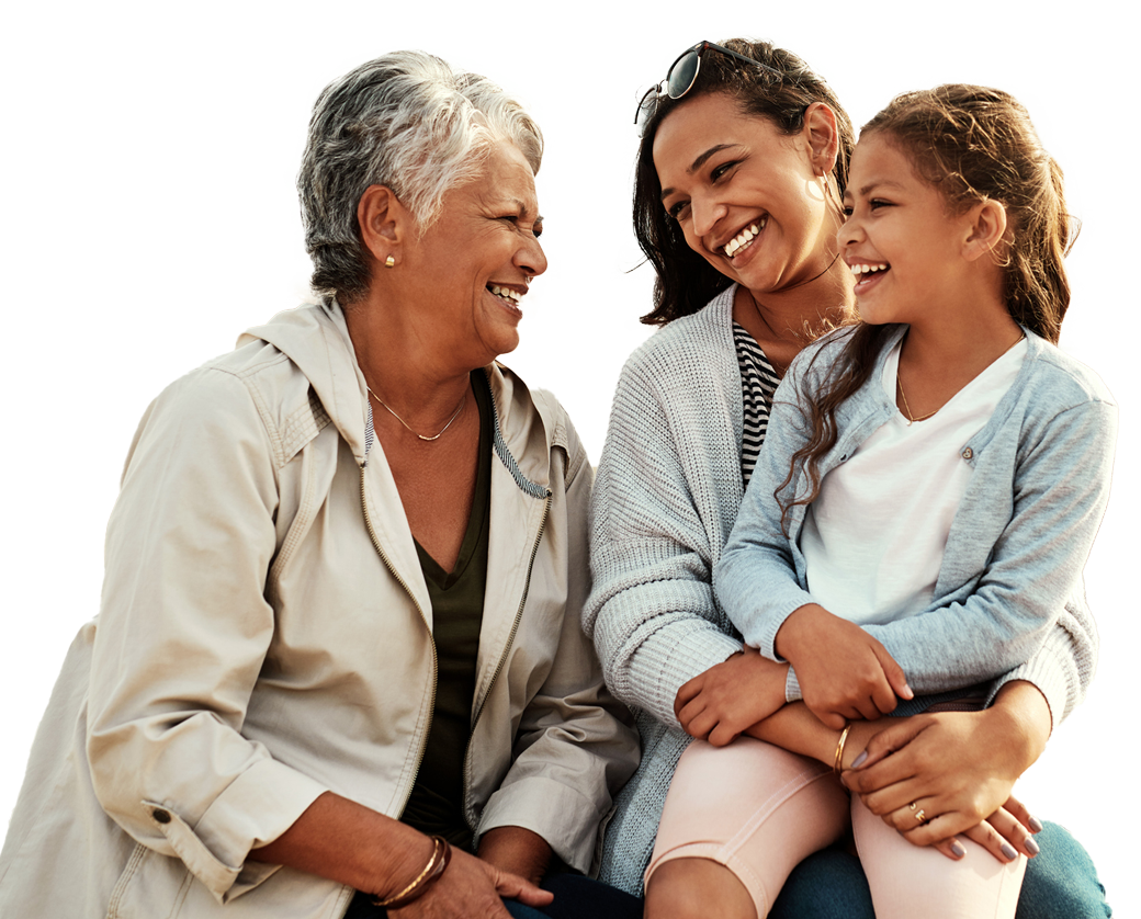 Three people of different generations smiling together outdoors on a sandy area