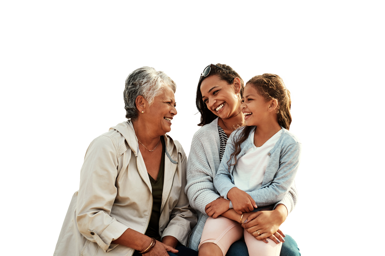 Three people of different generations smiling together outdoors on a sandy area