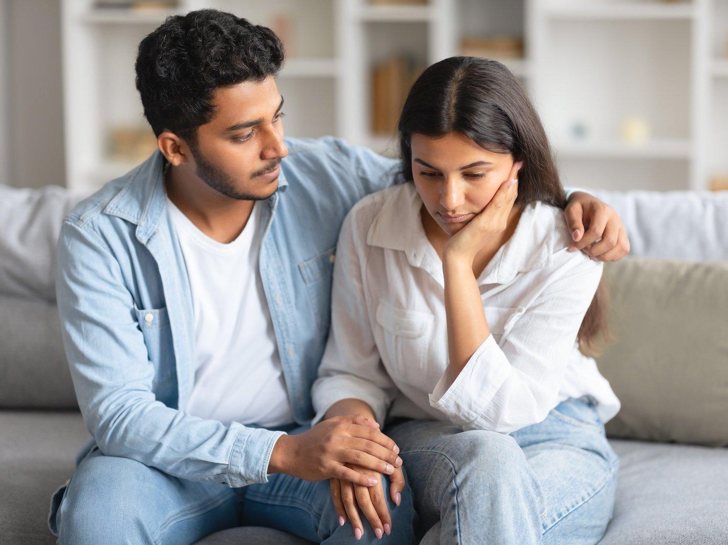 A man sitting with his arm around a women on a couch