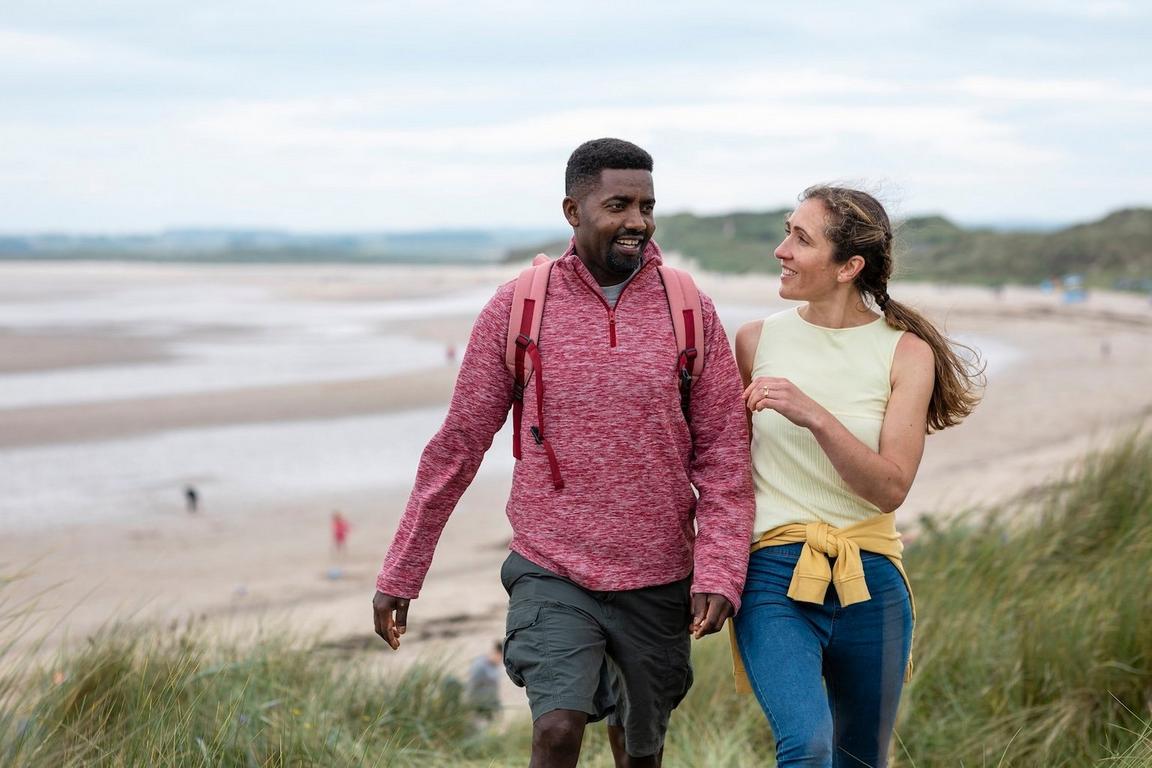 A man and woman walking together on a beach, smiling.
