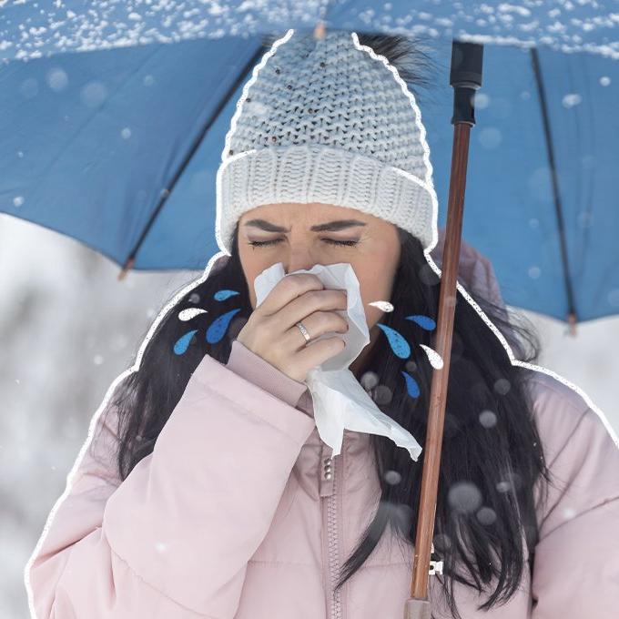 A woman blowing her nose holding a umbrella in the snow