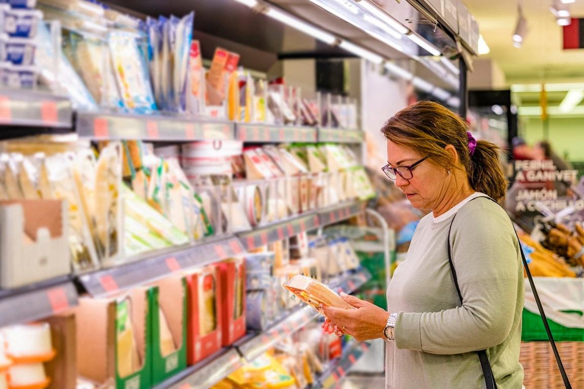 Woman examining a product in a grocery store aisle with refrigerated shelves.