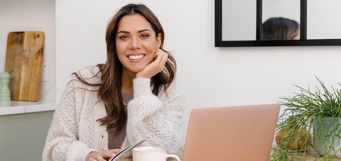 A woman smiling, sat at a table with a computer