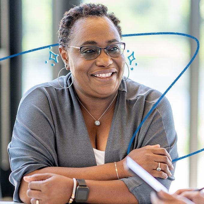 Person smiling with glasses and gray top, in a bright room with decorative blue lines.
