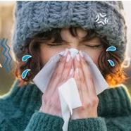 Someone blowing their nose into a tissue with closed eyes