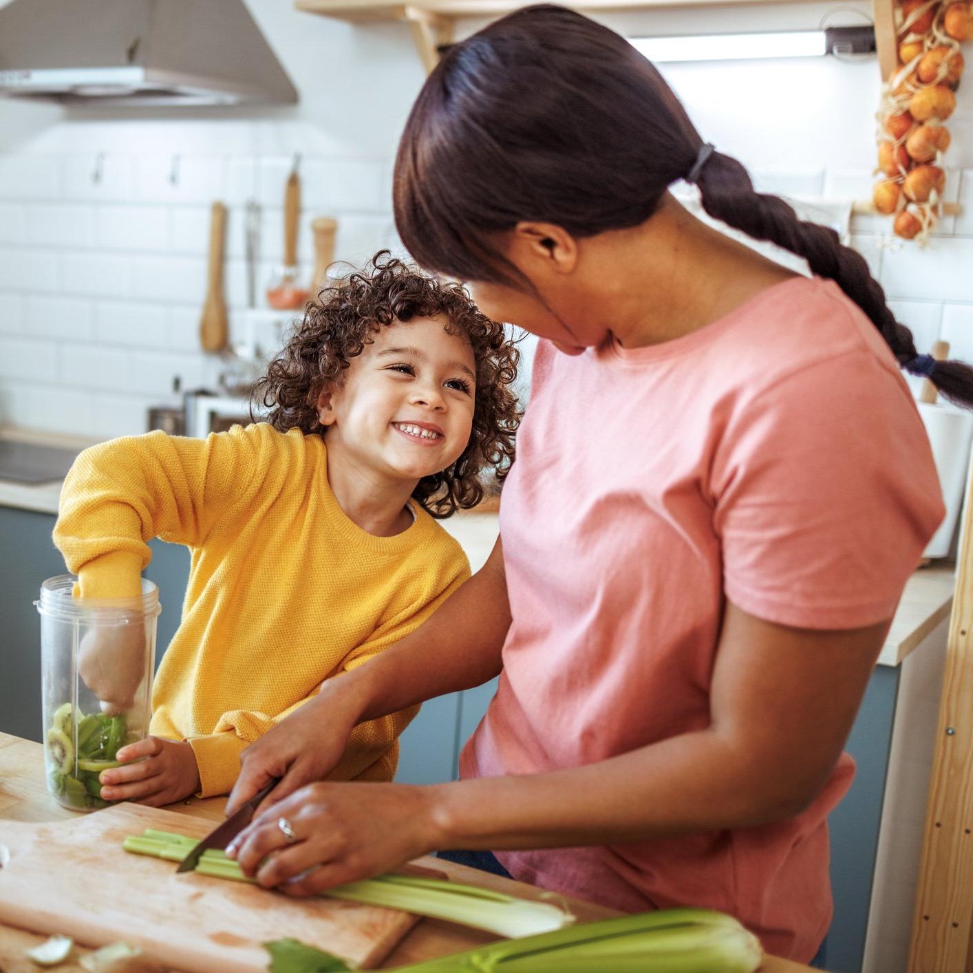 A woman and child in a kitchen, preparing food together with fruits and vegetables on the table