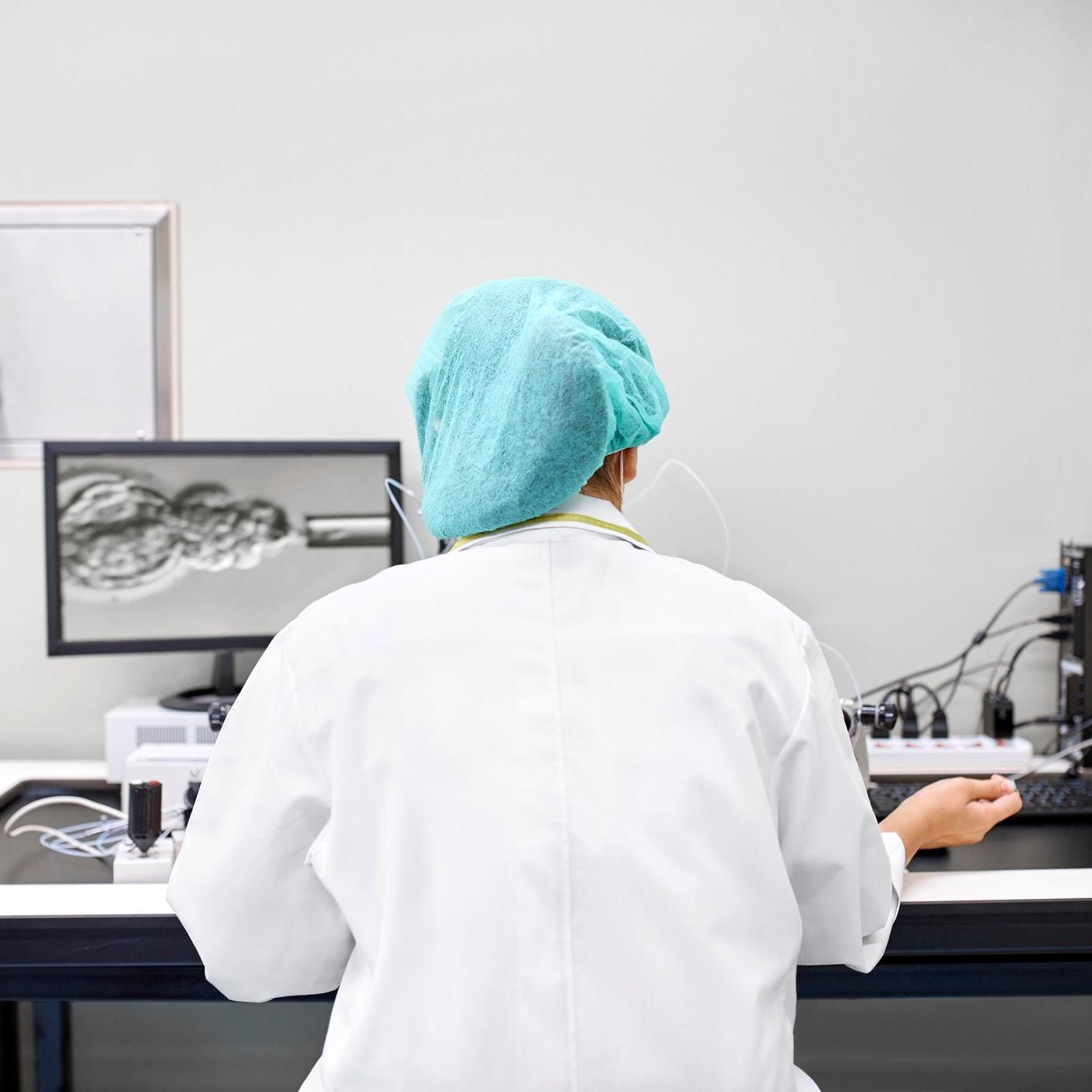 a lab technician in a lab coat sitting at a desk which has lab equipment