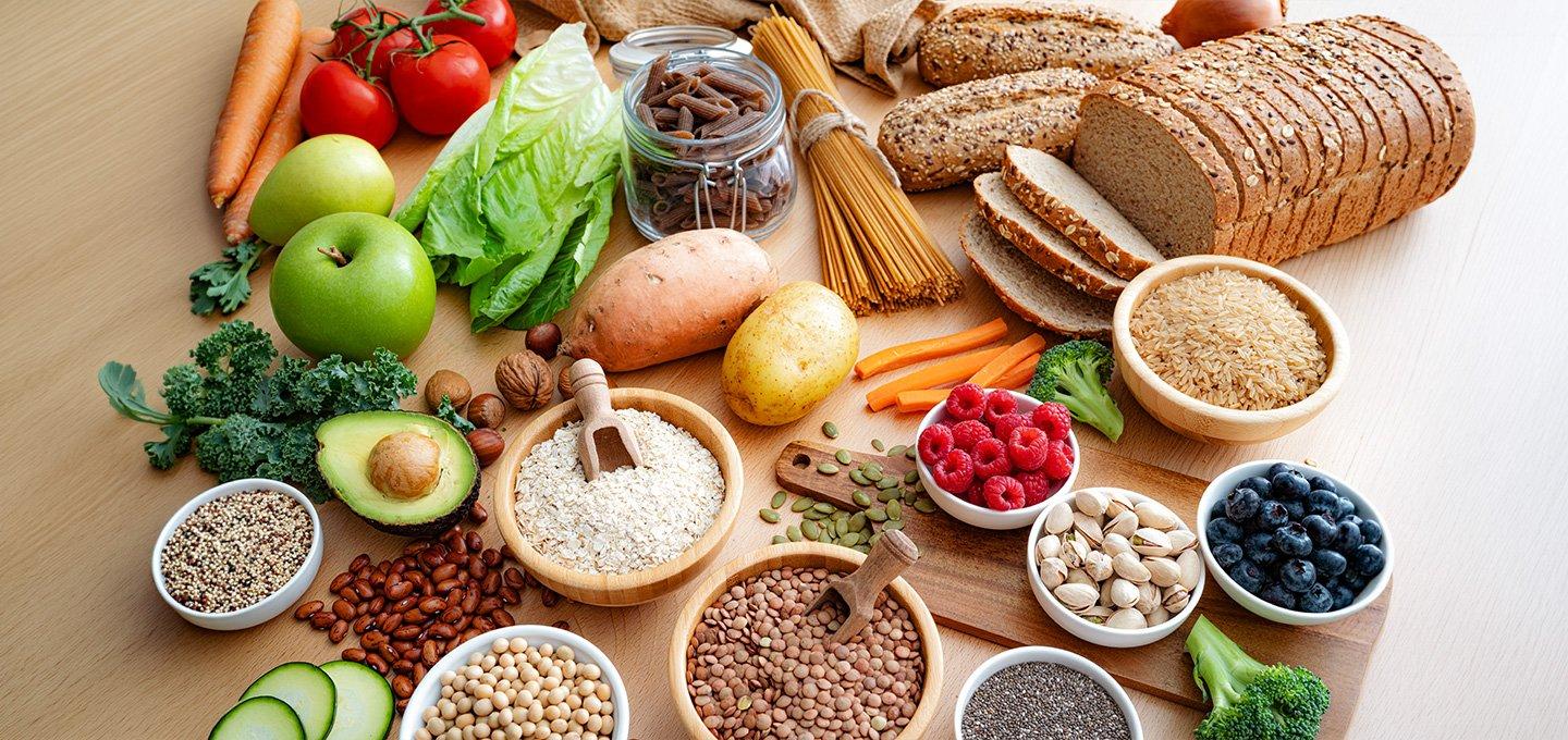 Selection of wholegrain, fruit, vegetable, legume, nut and seed foods arranged on a wooden table.