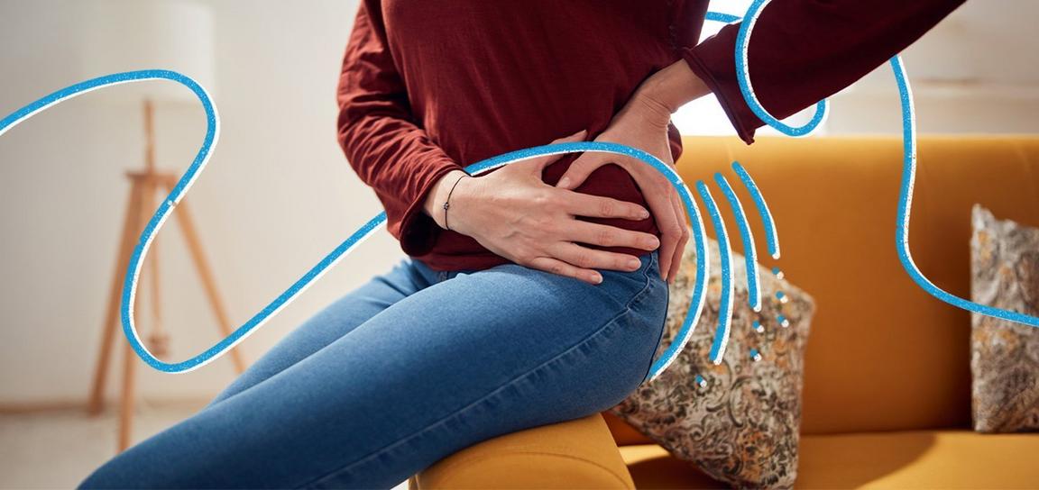 A person sat on the edge of a sofa holding their hip in pain