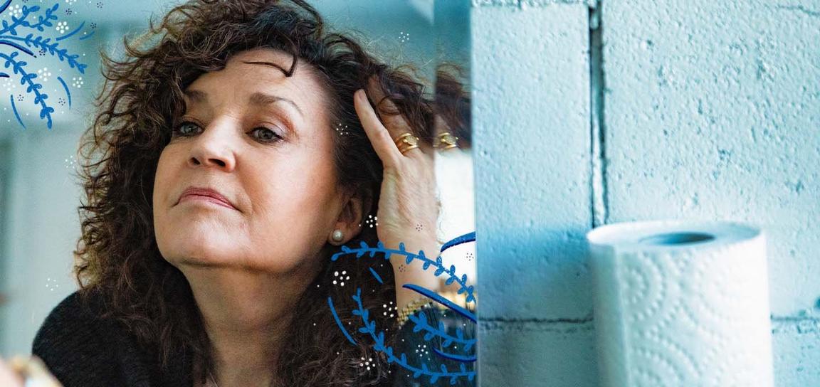 A woman with curly brown hair, touching her hair, with blue and white decorative patterns around her.