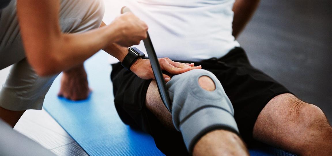 Close-up of a knee brace being adjusted by a therapist on a blue exercise mat.