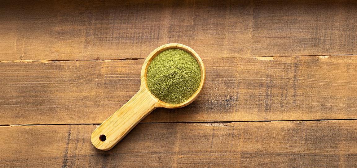 Wooden scoop filled with green powder on a wooden table.