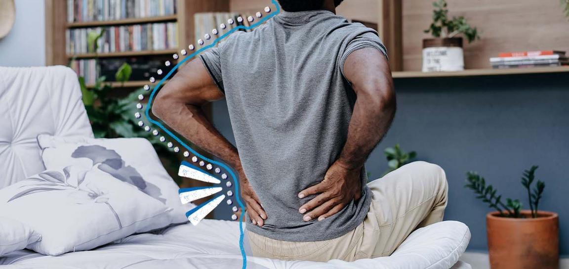 A man sitting down with his hands placed upon his lower back