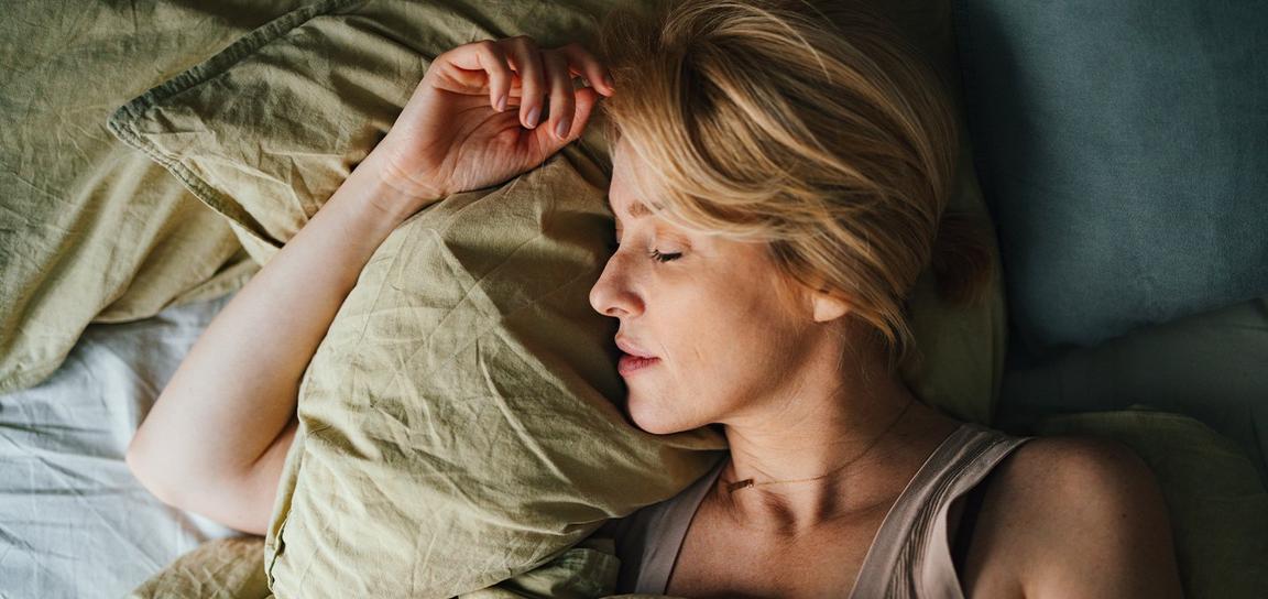 Woman sleeping on a bed with a light green pillow.