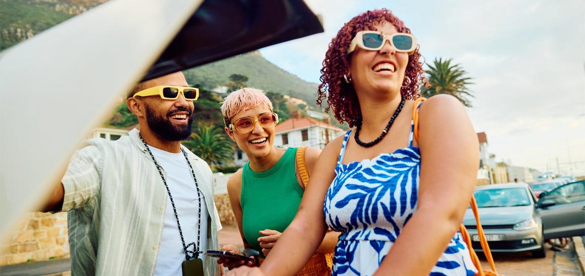 Group of three people smiling outdoors under a sunny sky.