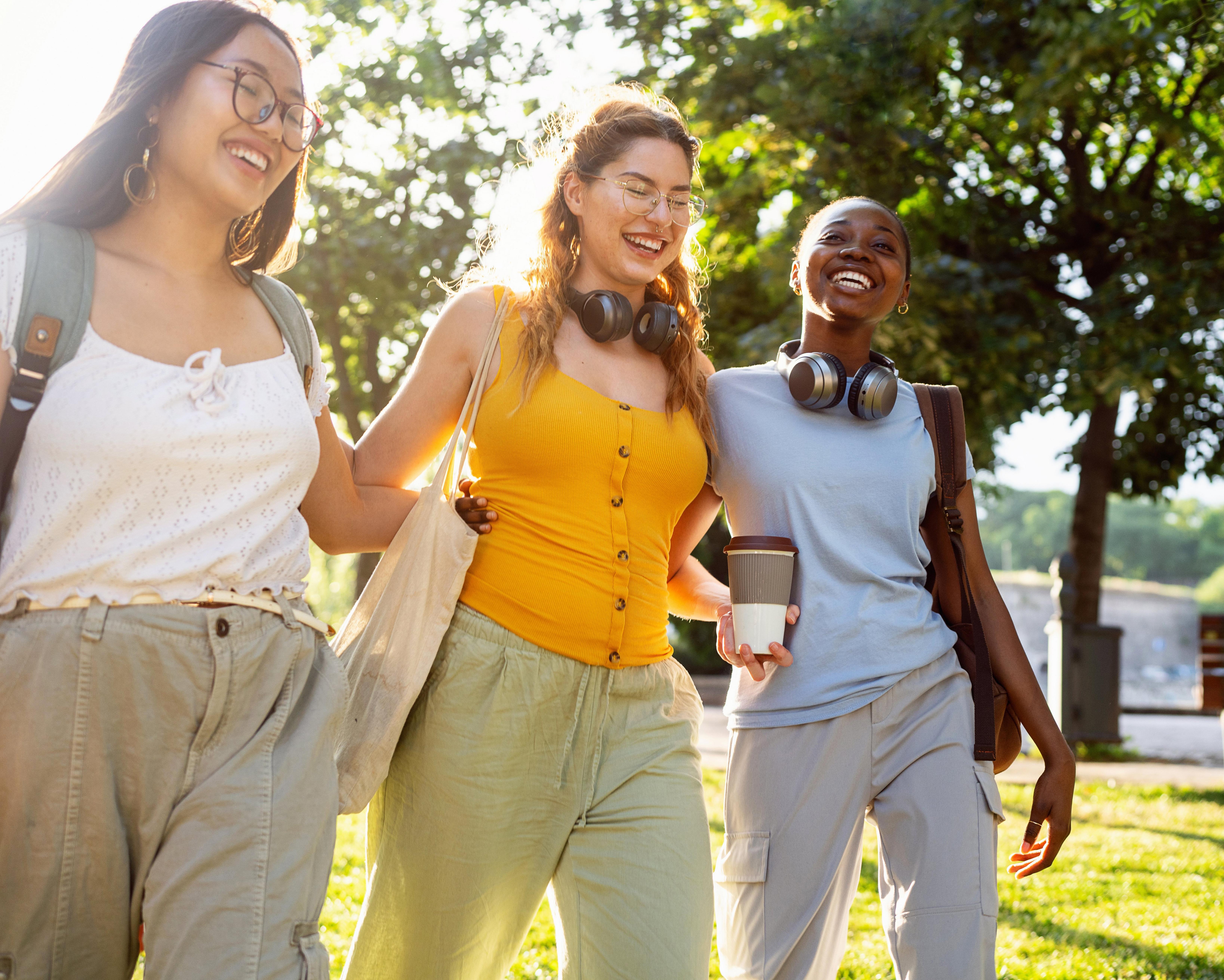 Three young adults walking outdoors, smiling, and wearing headphones around their necks.