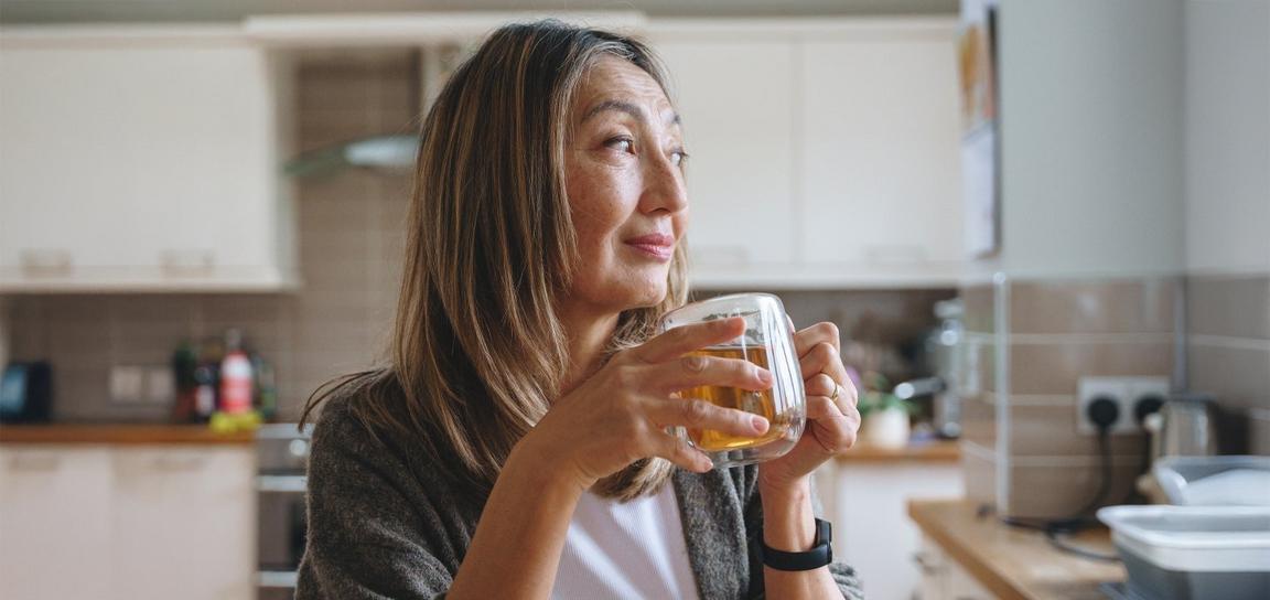 Person holding a mug in a kitchen, looking out the window.
