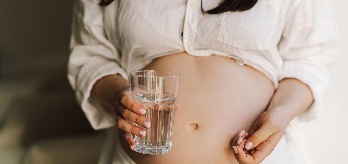 A pregnant woman holding a glass of water in their hand