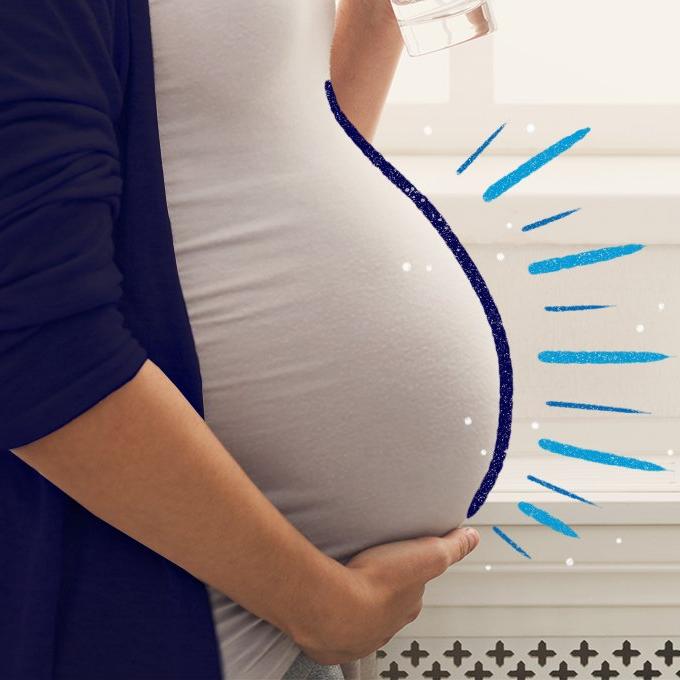 A pregnant woman holding their stomach while drinking a glass of water