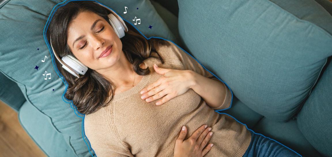 Someone lying on a blue sofa with their eyes closed, wearing headphones